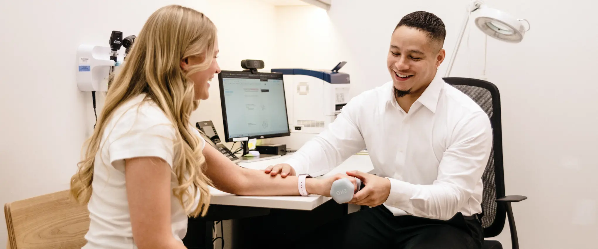 Male practitioner smiles while helping a female patient during a physical therapy session